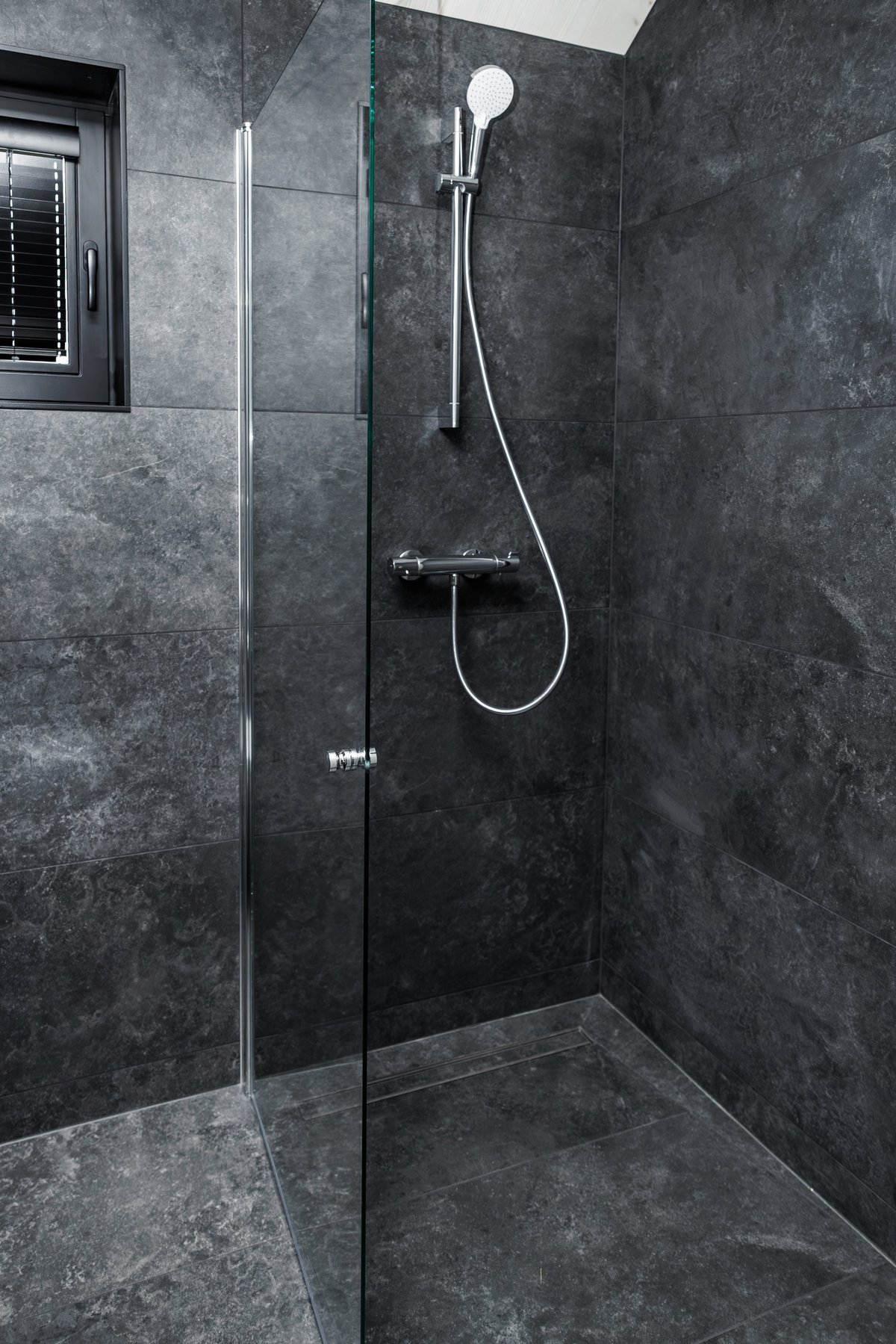 Modern walk-in shower with chrome fixtures and grey tiles