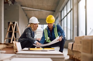 Construction worker and female real estate developer cooperating while examining construction plans at building site.