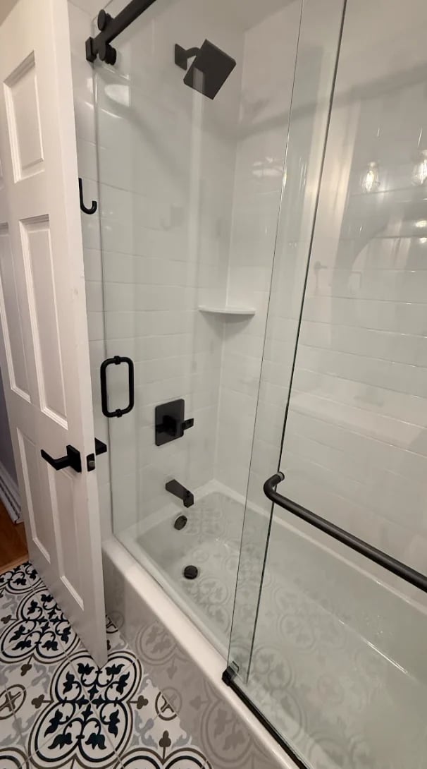 Modern glass-enclosed shower with white subway tile walls, black fixtures, and corner shelf in contemporary bathroom