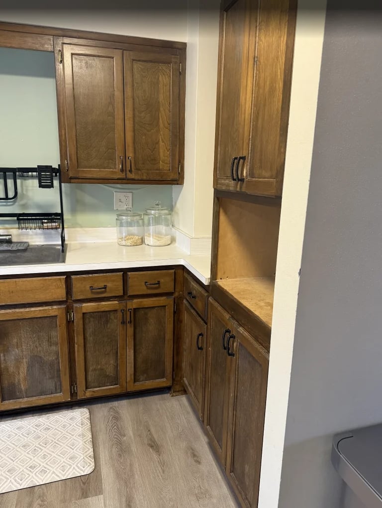 Kitchen corner with wooden cabinets, white countertops, glass cups, and light wood flooring