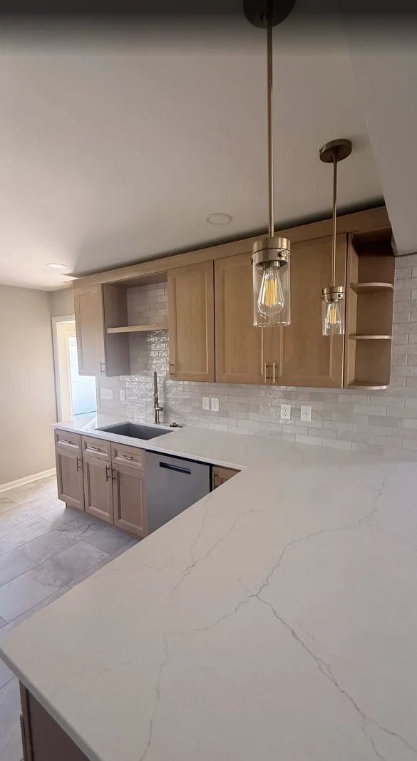 Modern kitchen with marble countertops, wood cabinetry, white subway tile backsplash, and pendant lights above island