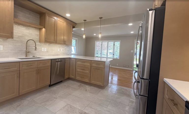 Modern kitchen with light wood cabinets, stainless steel appliances, white tile backsplash, and gray tile flooring