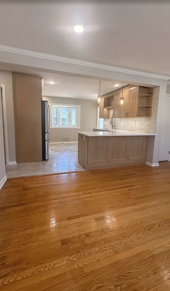 Modern kitchen and dining area with wood cabinetry, white subway tile backsplash, pendant lights, and hardwood flooring opening to living room