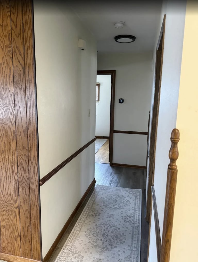 Long narrow hallway with wooden railings, white walls, gray ceiling, and light gray flooring