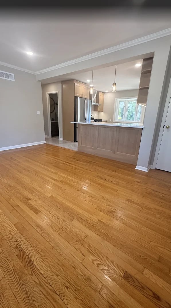 Open-concept kitchen and living room with wood flooring, modern island, pendant lights, and white cabinetry in new apartment