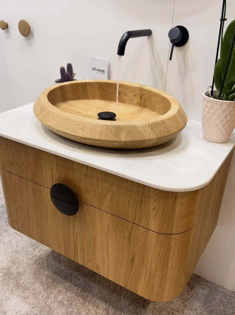 Modern wooden bathroom vanity with oval sink, white countertop, black faucet, and potted plant on the side
