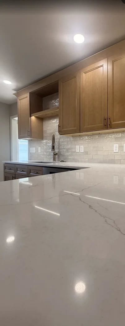 Modern kitchen with white marble countertops, wood cabinets, white subway tile backsplash, and recessed lighting fixtures in ceiling