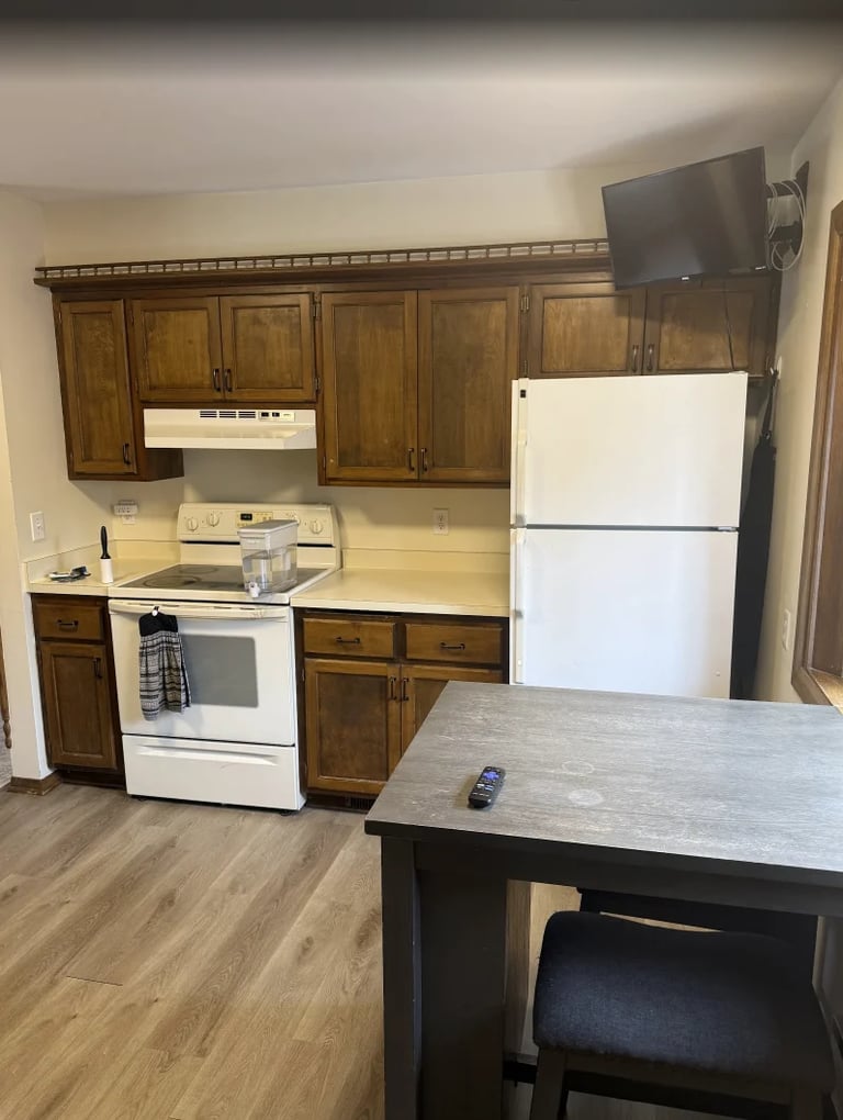 Kitchen with wooden cabinets, white appliances, island with seating, and TV mounted on wall