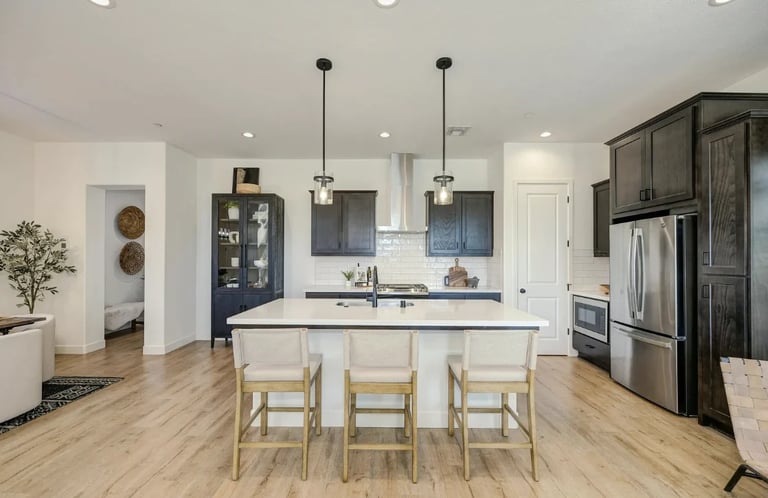 Modern kitchen with white island, wooden bar seating, pendant lights, stainless steel appliances, and light wood flooring