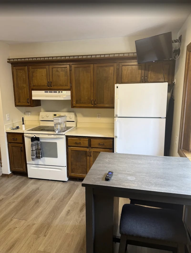 Kitchen with white appliances, wood cabinets, island with seating, mounted TV, and hardwood flooring