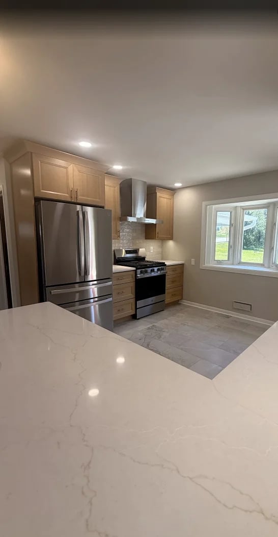 Modern kitchen with white marble countertop, stainless steel appliances, wood cabinets, and windows overlooking yard